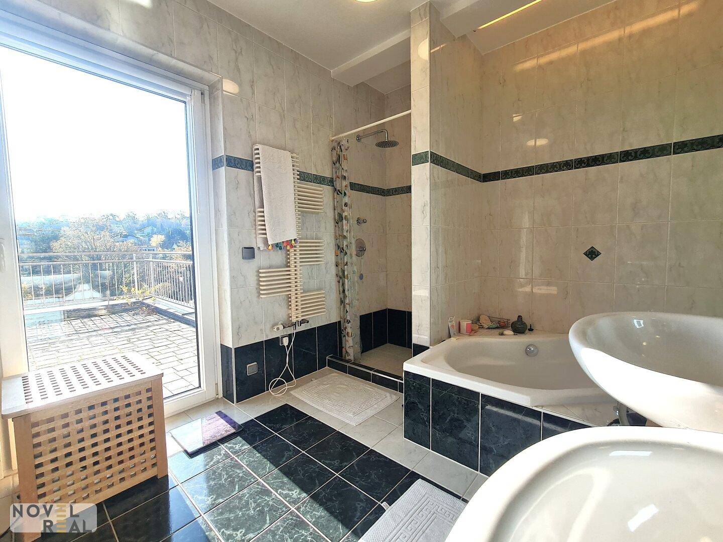 Gefliestes Badezimmer mit Badewanne, Dusche und Zugang zu einer Außenterrasse.