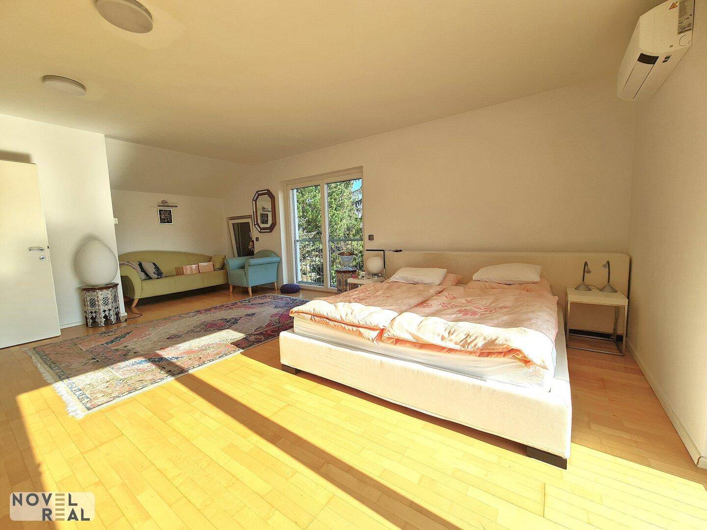 Geräumiges Schlafzimmer mit Doppelbett, Sitzbereich und viel Tageslicht durch große Fenster.
