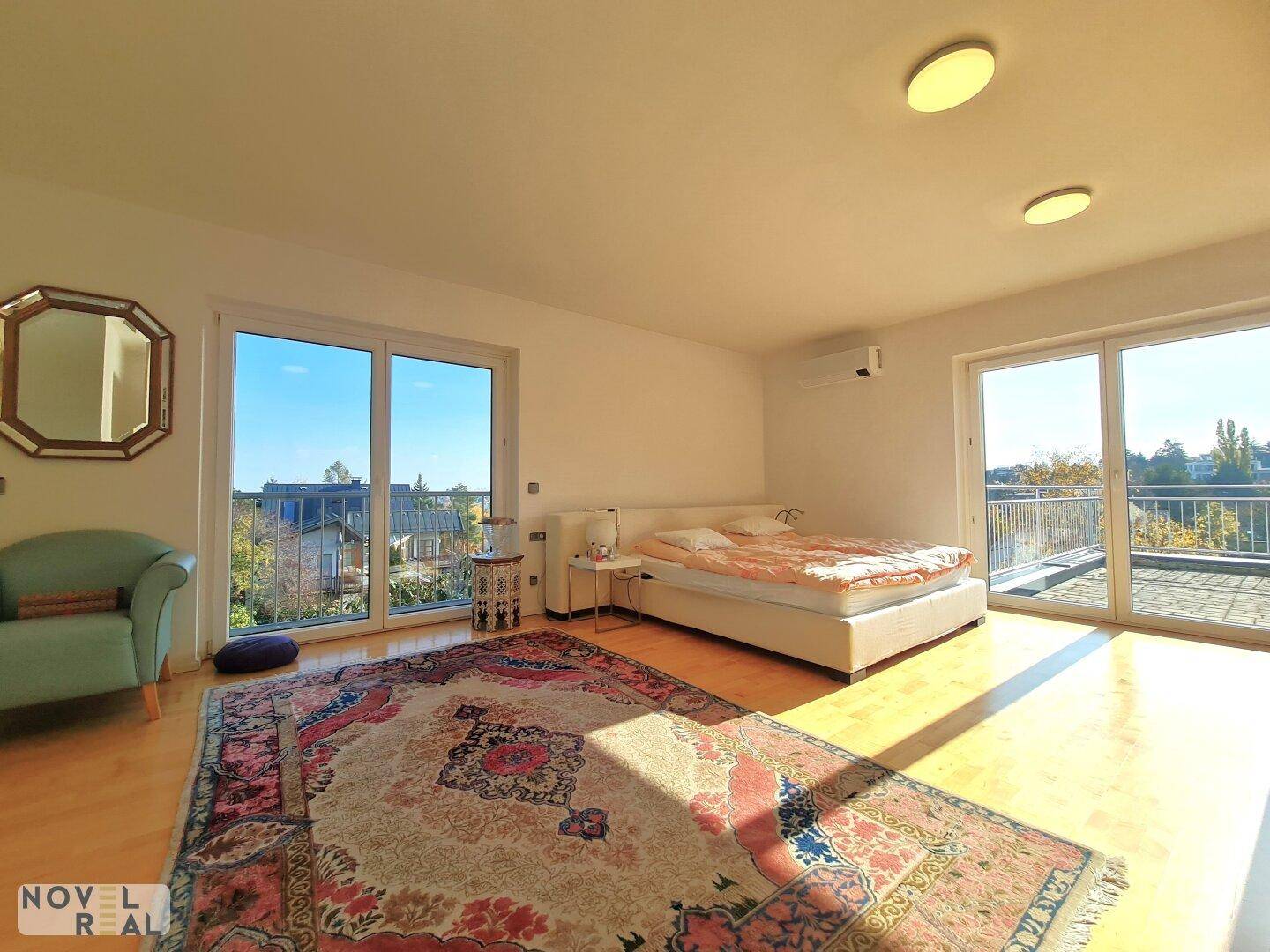 Helles Schlafzimmer mit Doppelbett, Teppich und Zugang zu einer großen Terrasse.
