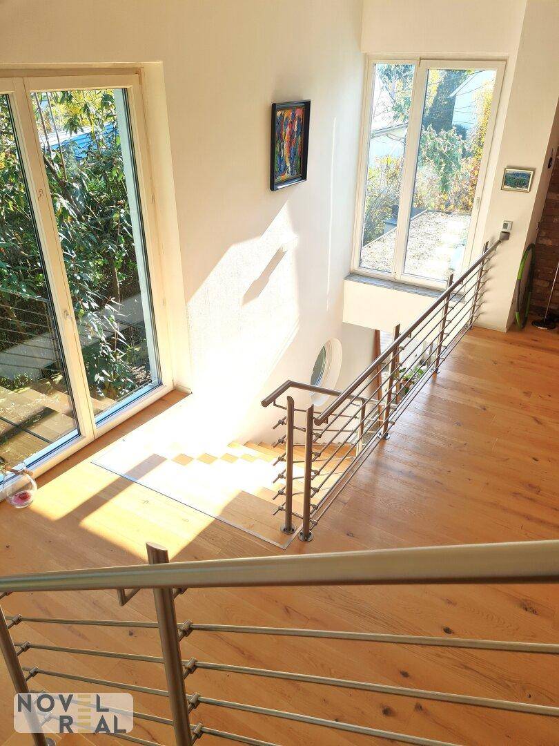 Moderne Holztreppe mit Edelstahlgeländer in einem hellen, lichtdurchfluteten Bereich.