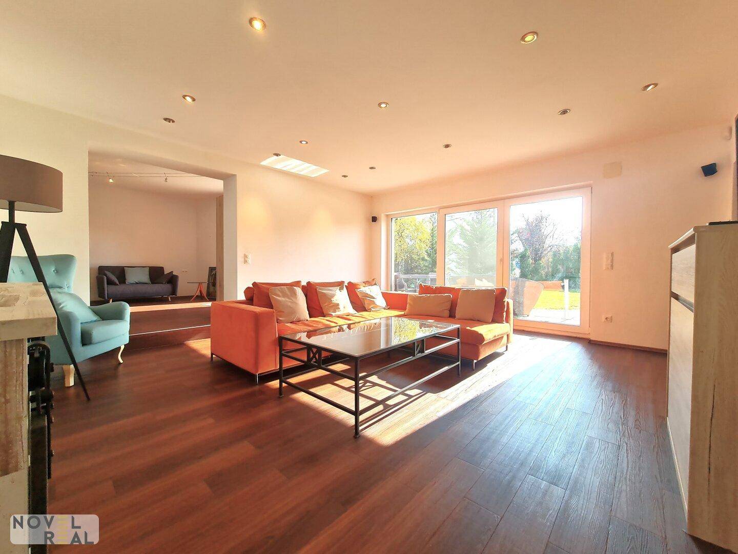 Geräumiges Wohnzimmer mit modernem Sofa, dunklem Holzboden und viel Tageslicht.