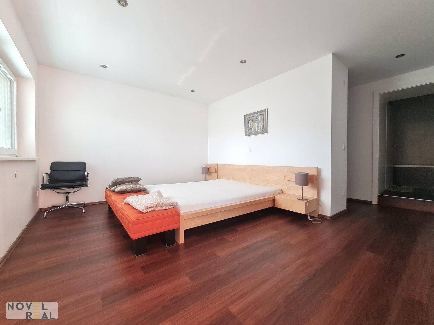Helles Schlafzimmer mit Holzbett, dunklem Holzboden und einem Fenster.