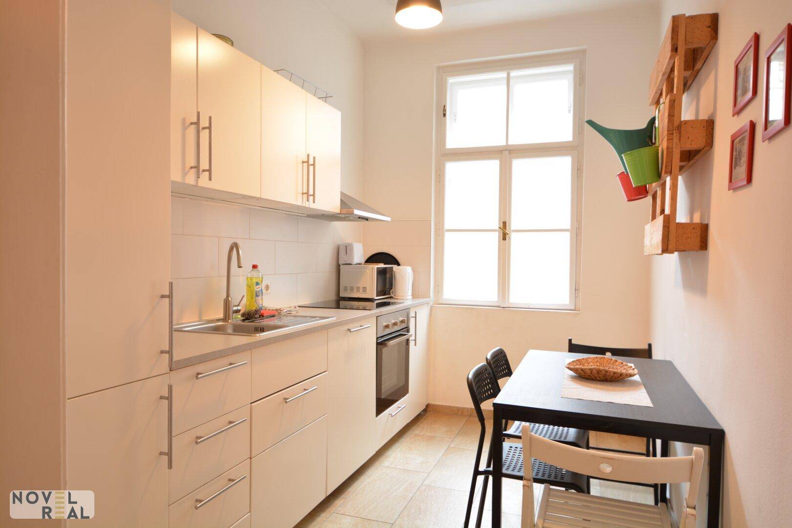 Helle Küche mit weißen Schränken, Esstisch und Fenster, ausgestattet mit Mikrowelle und Ofen.
