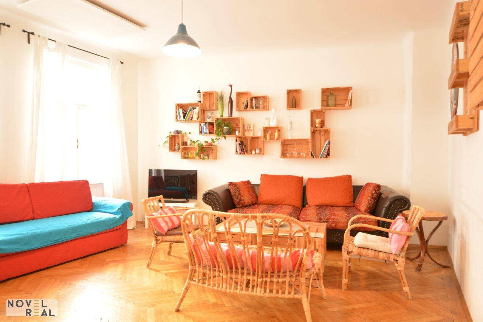 Geräumiges Wohnzimmer mit Sofa, Rattansesseln, Holzboden und kreativer Wanddekoration.