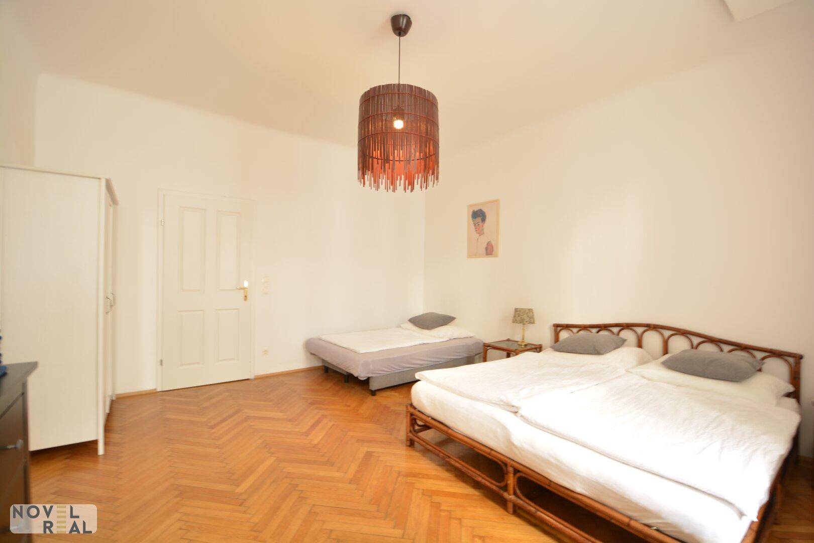 Schlafzimmer mit Holzboden, zwei Betten und einem weißen Kleiderschrank neben der Zimmertür.