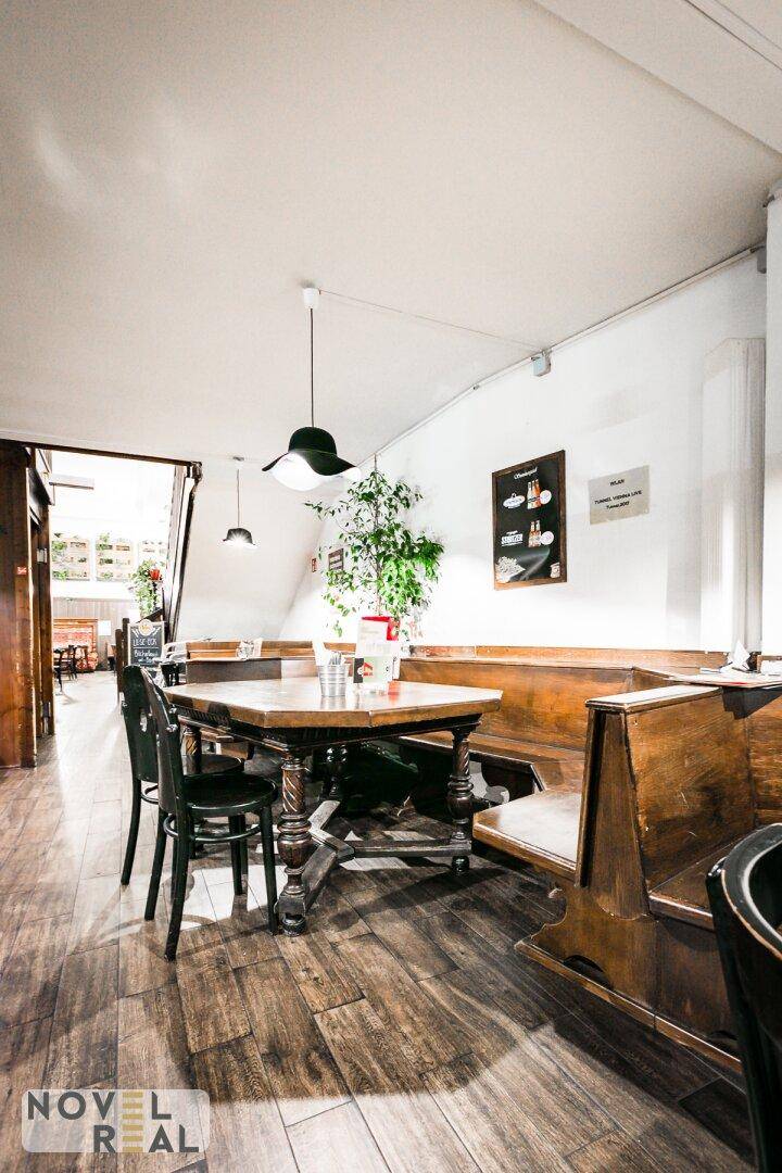 Gemütlicher Restaurantbereich mit Holztischen, Bänken und Stühlen, beleuchtet von einer Hängelampe.