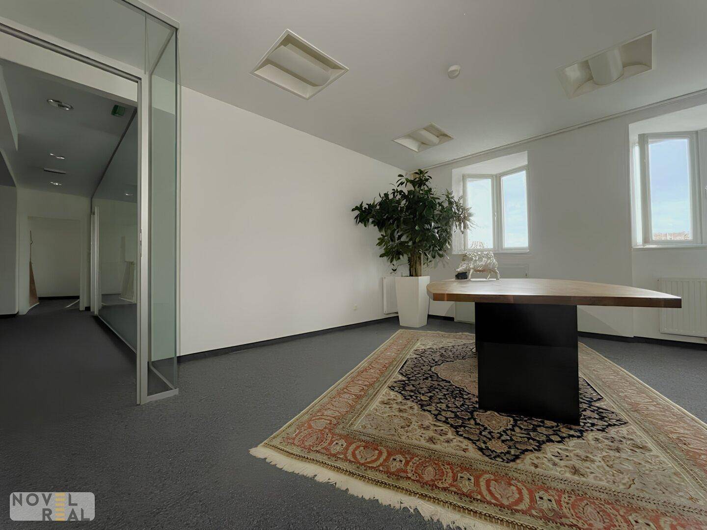 Geräumiges Büro mit Teppichboden, modernem Tisch und Blick durch Glaswände in den Flur.