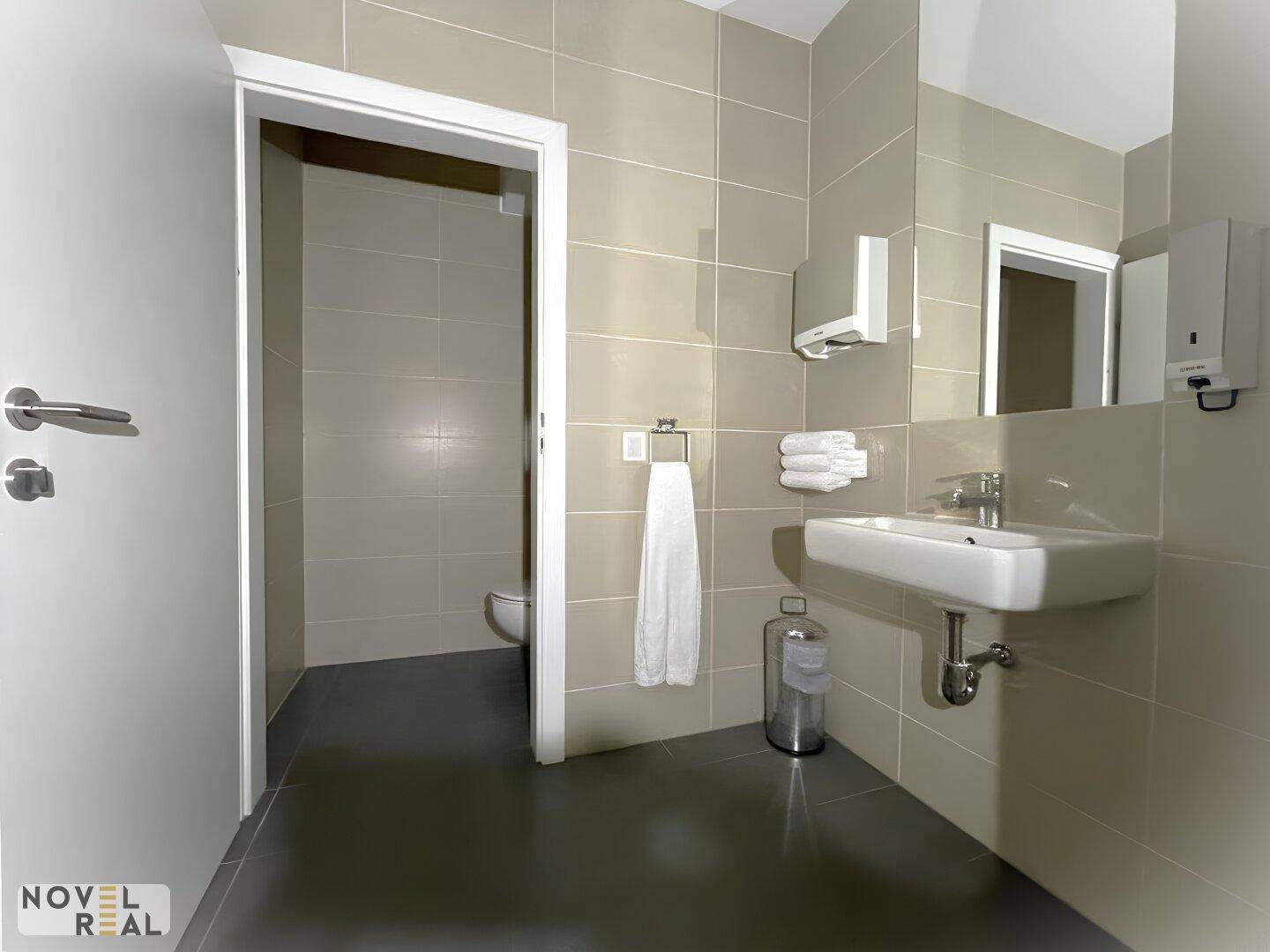 Sauberes Badezimmer mit beigen Wandfliesen, Waschbecken und Zugang zur Toilette.