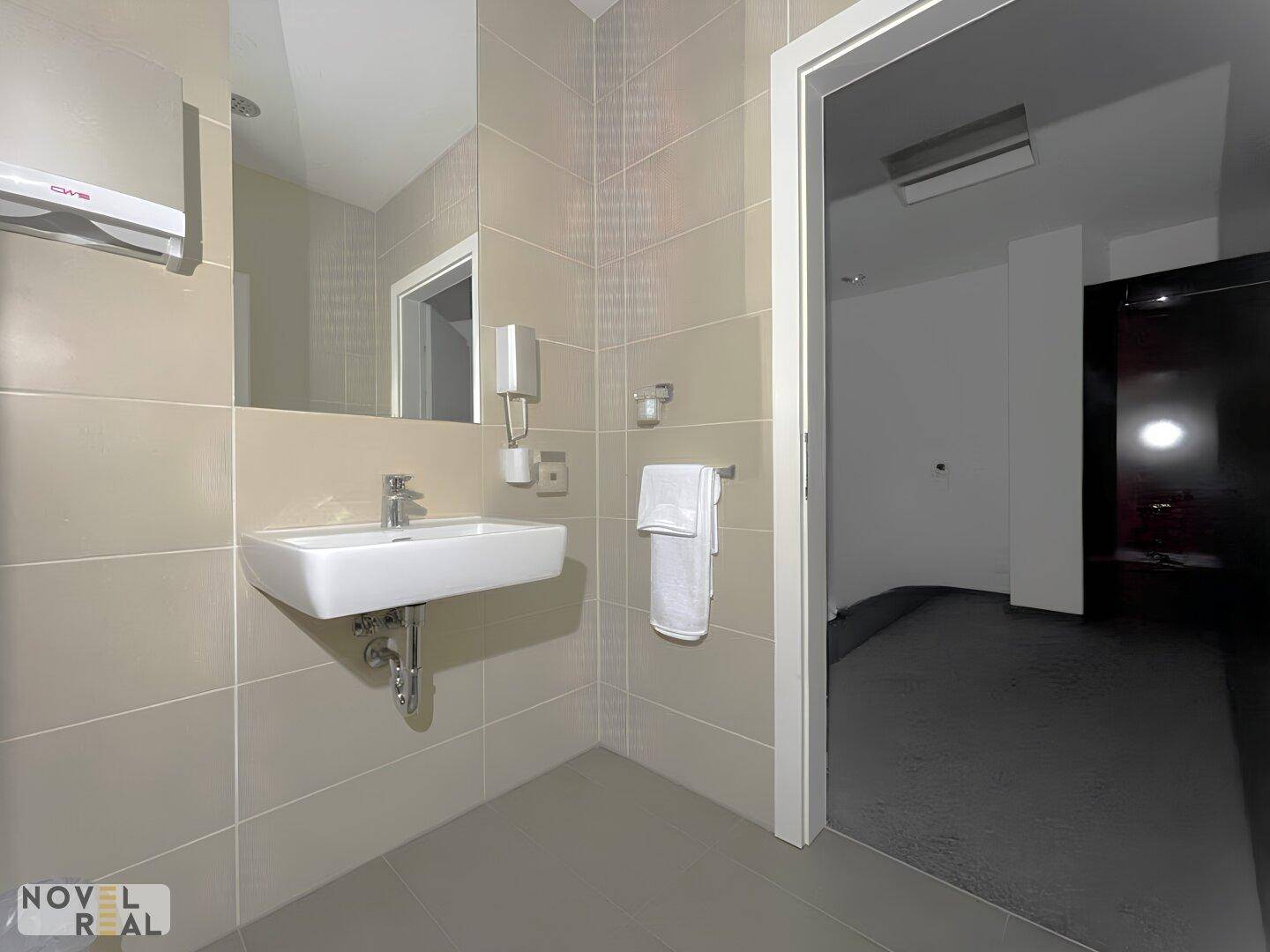 Modernes Badezimmer mit beigen Fliesen, Waschbecken und Spiegel, gut beleuchtet.