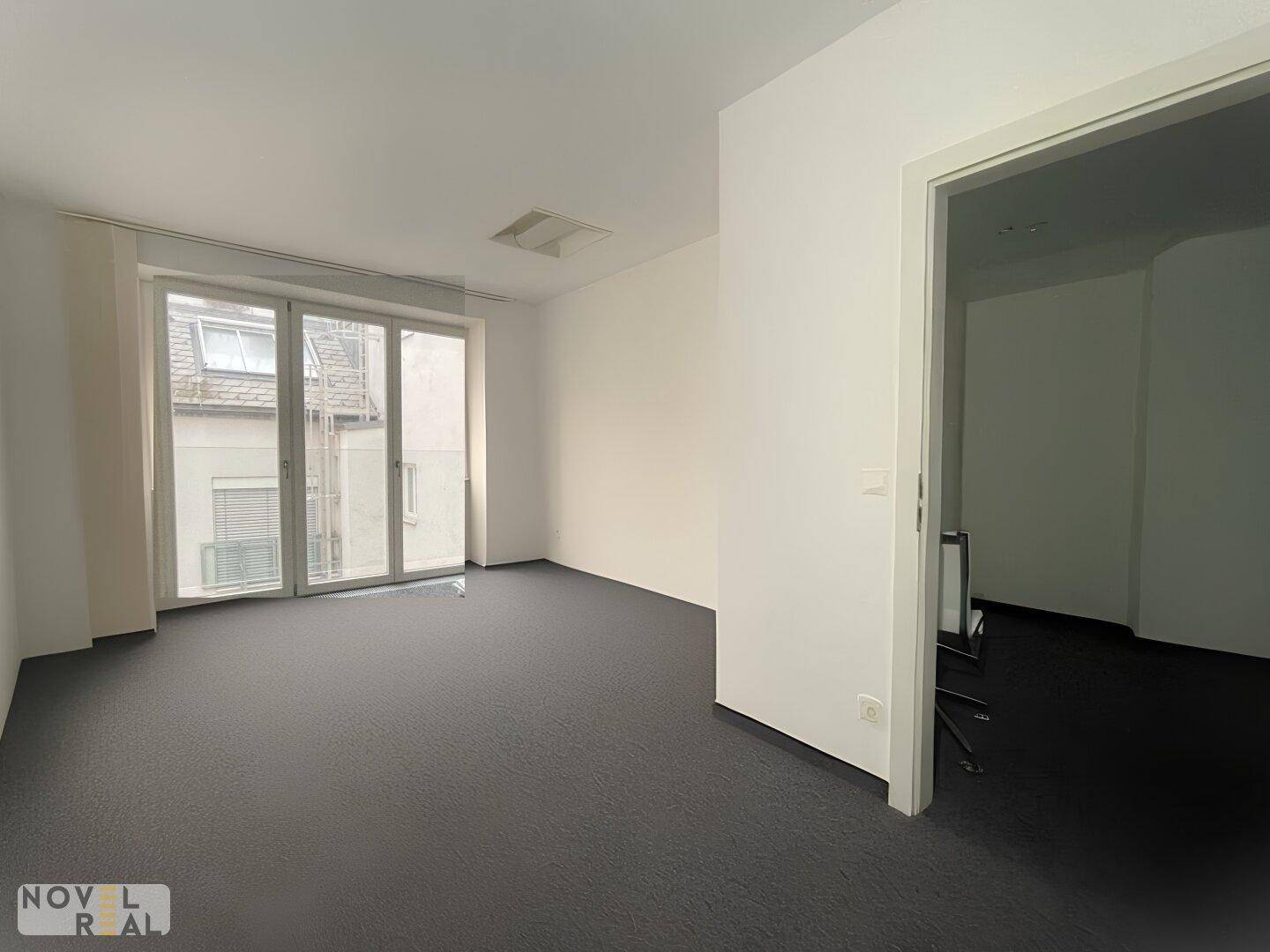 Helles Einzelbüro mit Teppichboden und großen Fenstern, die viel Tageslicht hereinlassen.