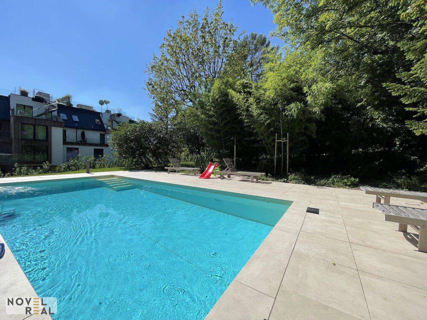 Großer Außenpool mit klarem Wasser, umgeben von einer hellen Terrasse und Liegestühlen.