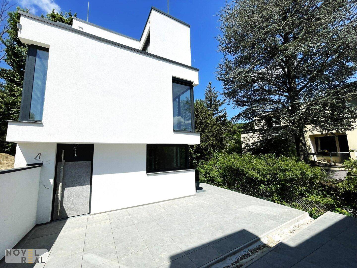 Zeitgenössisches Gebäude mit weißer Fassade und einer gepflasterten Fläche im Freien.
