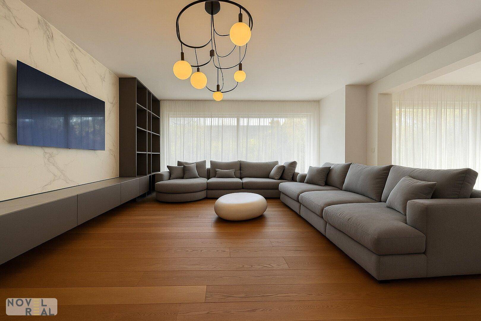 Modernes Wohnzimmer mit großem Sofa, Marmorwand und bodentiefen Fenstern für viel Tageslicht.