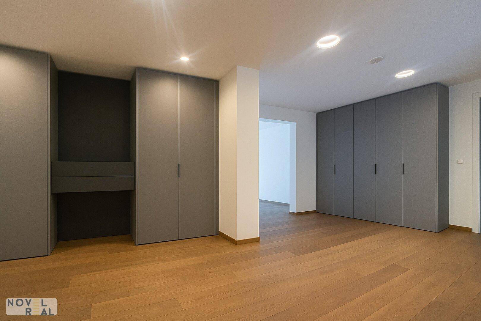 Geräumiges Schlafzimmer mit eleganten grauen Einbauschränken und warmem Holzfußboden.