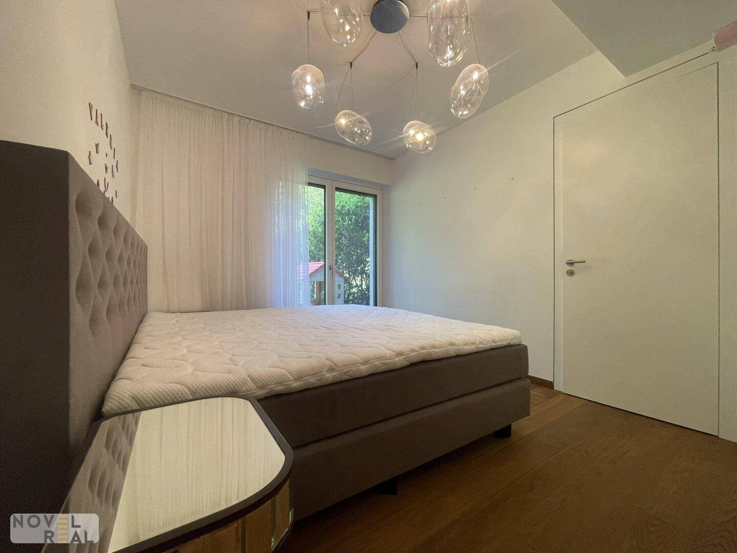 Helles Schlafzimmer mit großem Bett und Zugang zu einem Außenbereich durch eine Glastür.