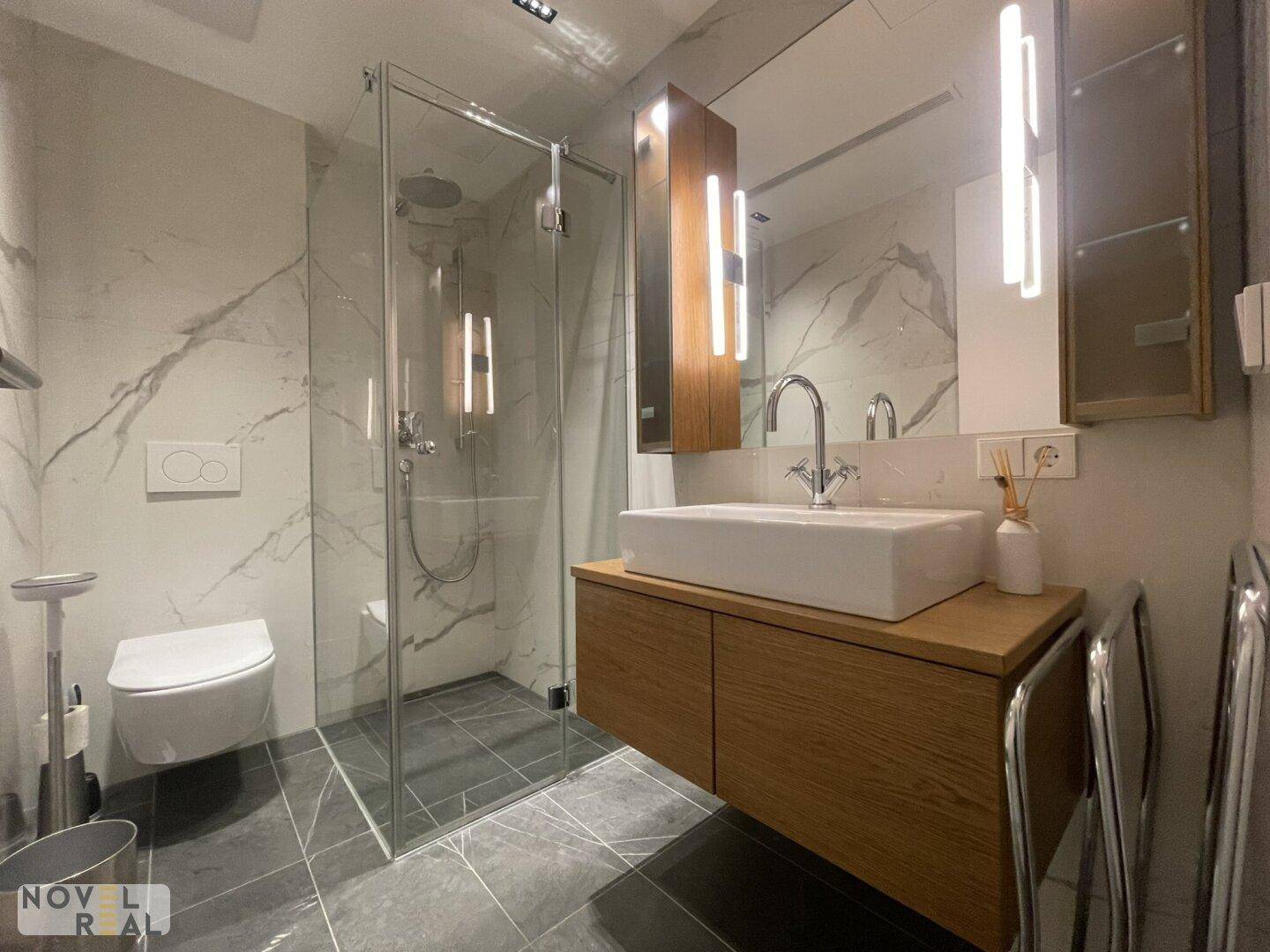 Modernes Badezimmer mit Waschtisch, wandhängendem WC und begehbarer Dusche, elegant gefliest.