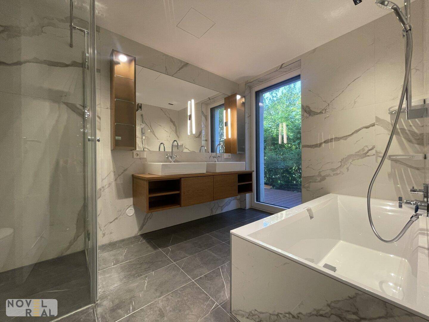 Luxuriöses Badezimmer mit Doppelwaschbecken, Badewanne, begehbarer Dusche und großem Fenster.