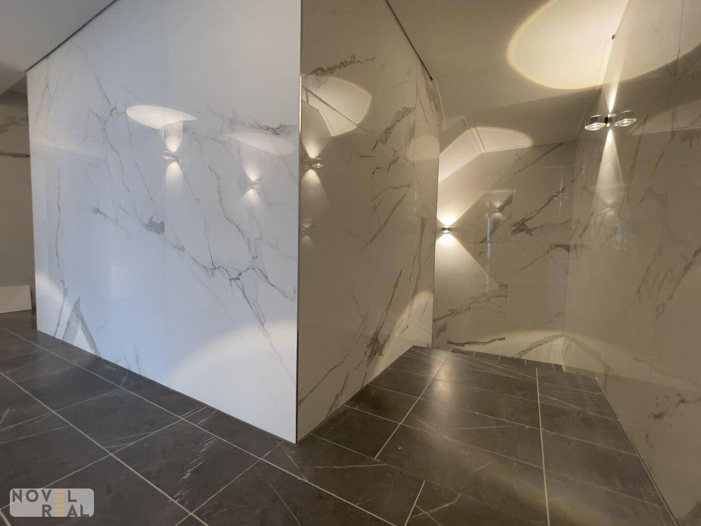 Modernes Badezimmer mit großformatigen Marmorfliesen an den Wänden und dunklem Fliesenboden.