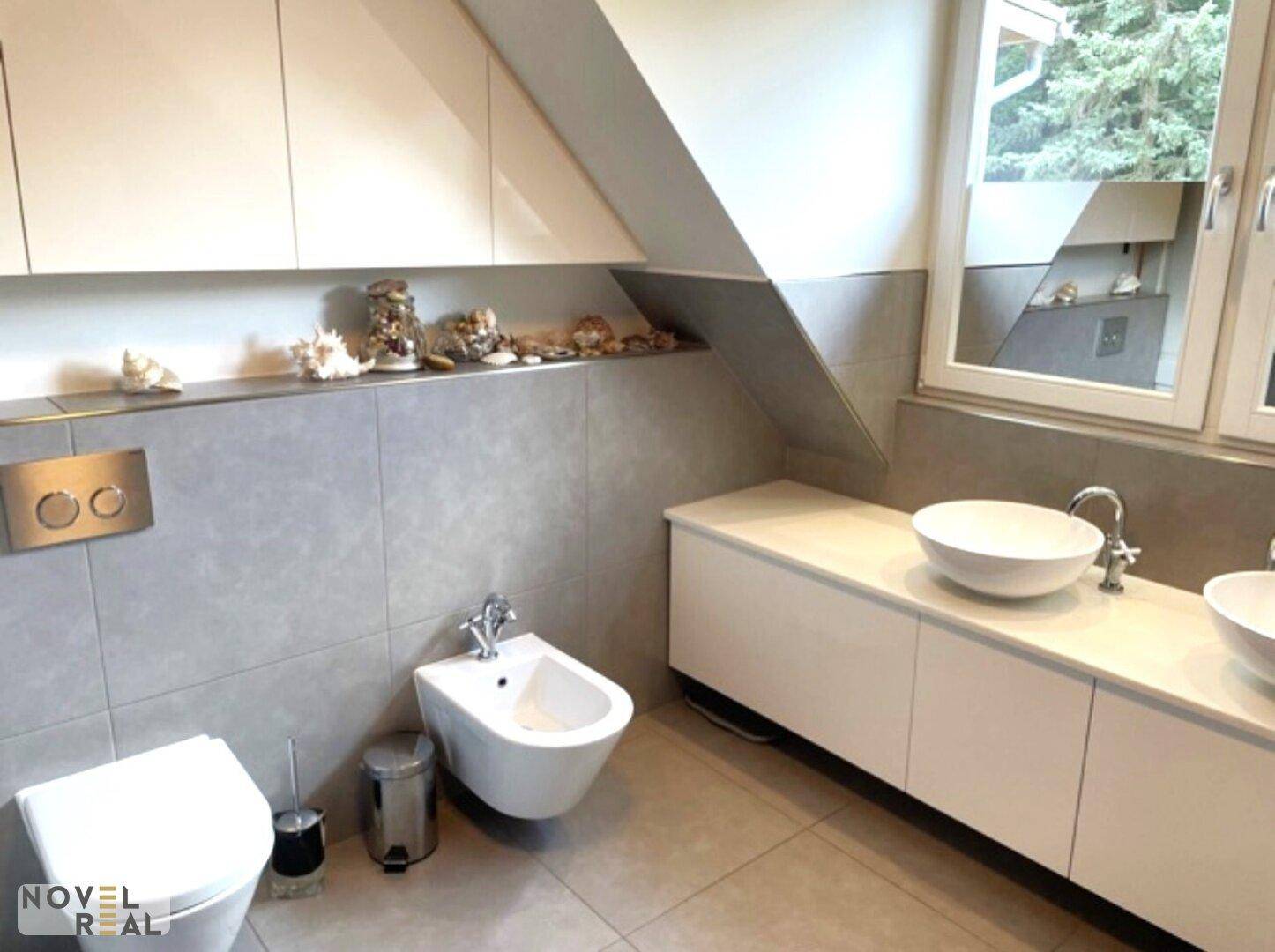 Helles Badezimmer mit Toilette, Bidet, Doppelwaschbecken und einem Fenster für Tageslicht.