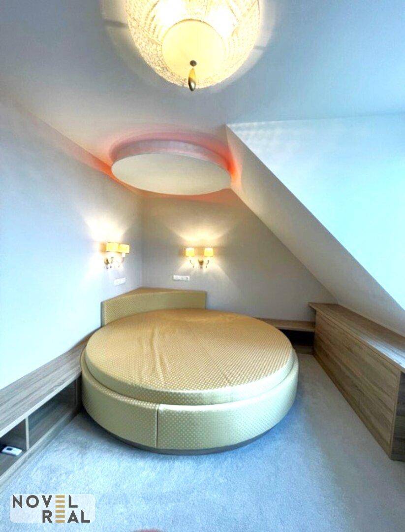 Gemütliches Schlafzimmer mit rundem Bett und indirekter Beleuchtung unter Dachschrägen.