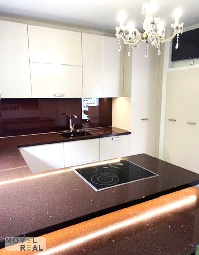Moderne Küche mit dunklen Arbeitsplatten, weißen Schränken und einem eleganten Kronleuchter.