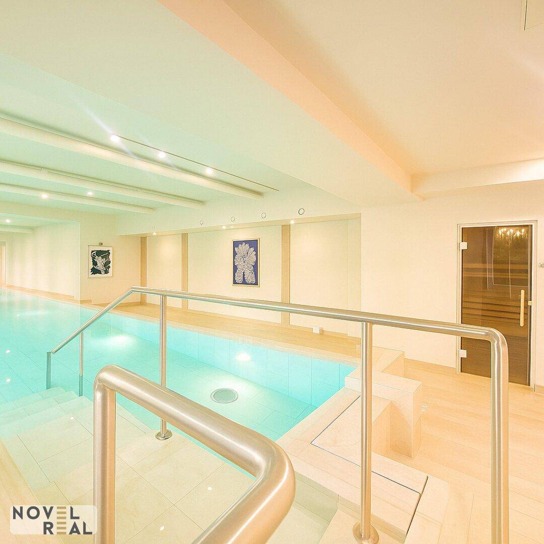 Innenpoolbereich mit Zugang zur Sauna, hellen Fliesen und modernen Handläufen für Komfort.
