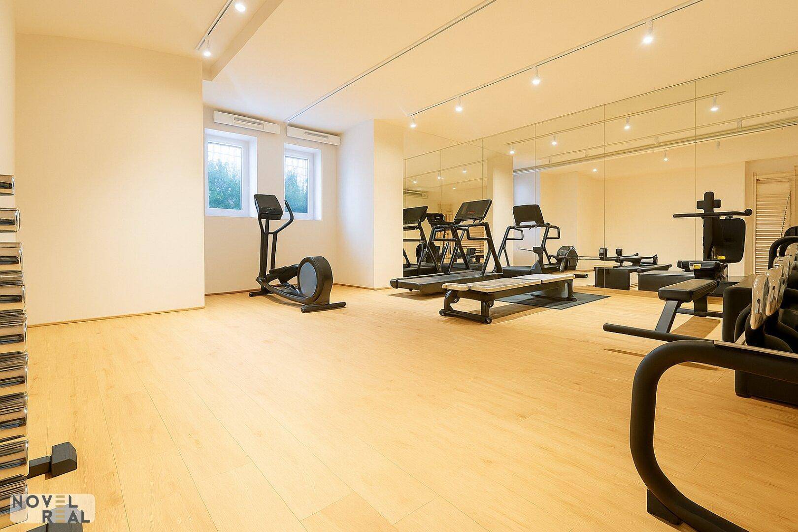 Gut ausgestatteter Fitnessraum mit verschiedenen Trainingsgeräten, Spiegelwänden und Parkettboden.