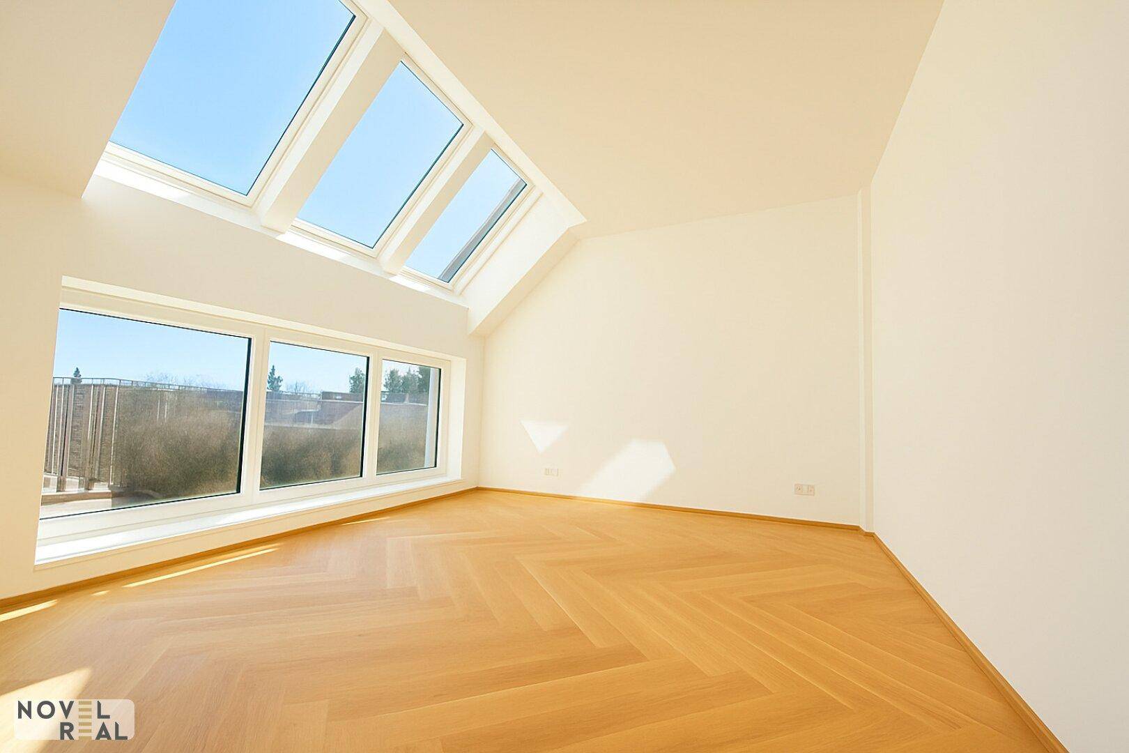 Heller Raum mit Fischgrätparkett, Dachfenstern und großen Fenstern, die viel Licht spenden.