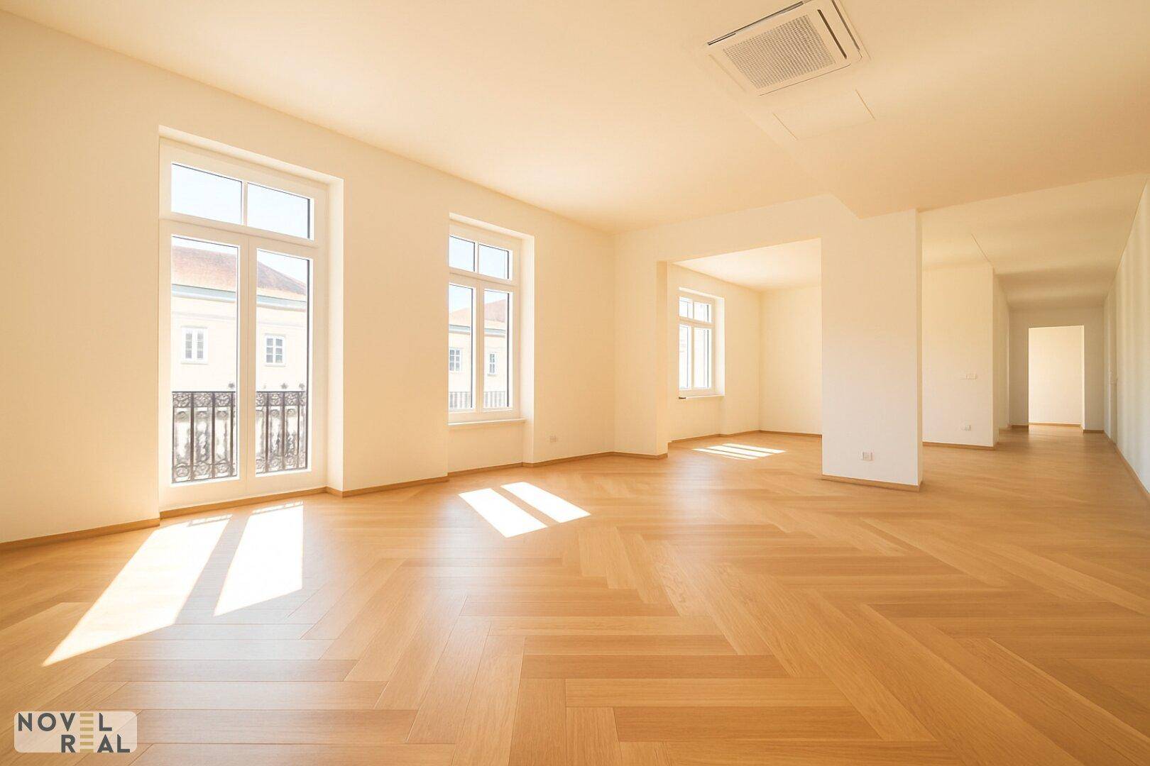 Geräumiges Wohnzimmer mit Fischgrätparkett, hohen Decken und großen Fenstern mit französischem Balkon.