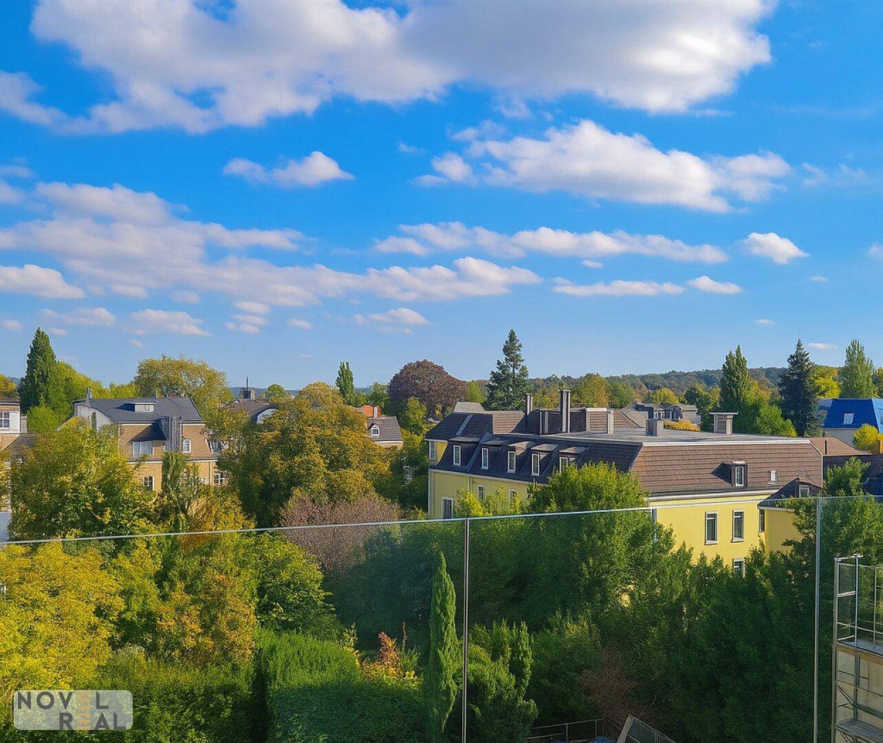 Weitläufiger Blick über eine grüne Wohngegend mit Bäumen und Dächern unter blauem Himmel.