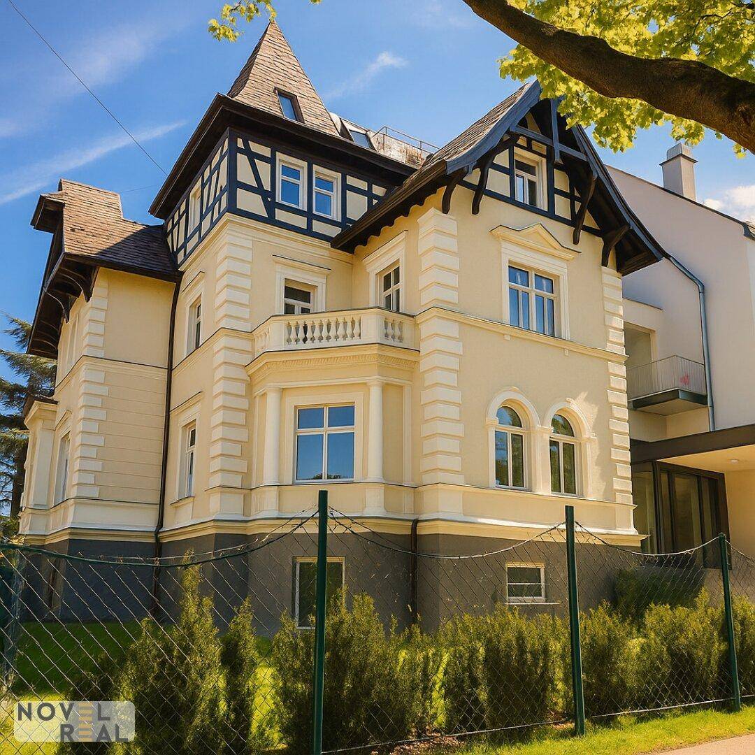 Klassisches Gebäude mit eleganter Fassade, Spitzdach und gepflegtem Vorgarten unter blauem Himmel.
