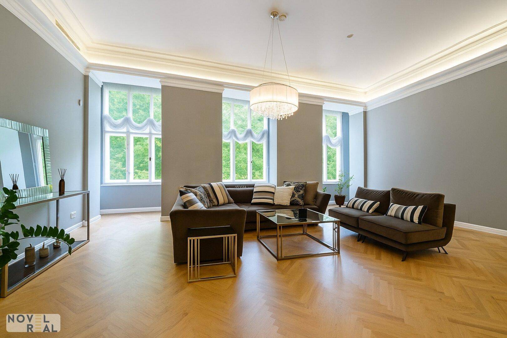 Großzügiges Wohnzimmer mit Fischgrätparkett, hohen Decken und Blick ins Grüne.