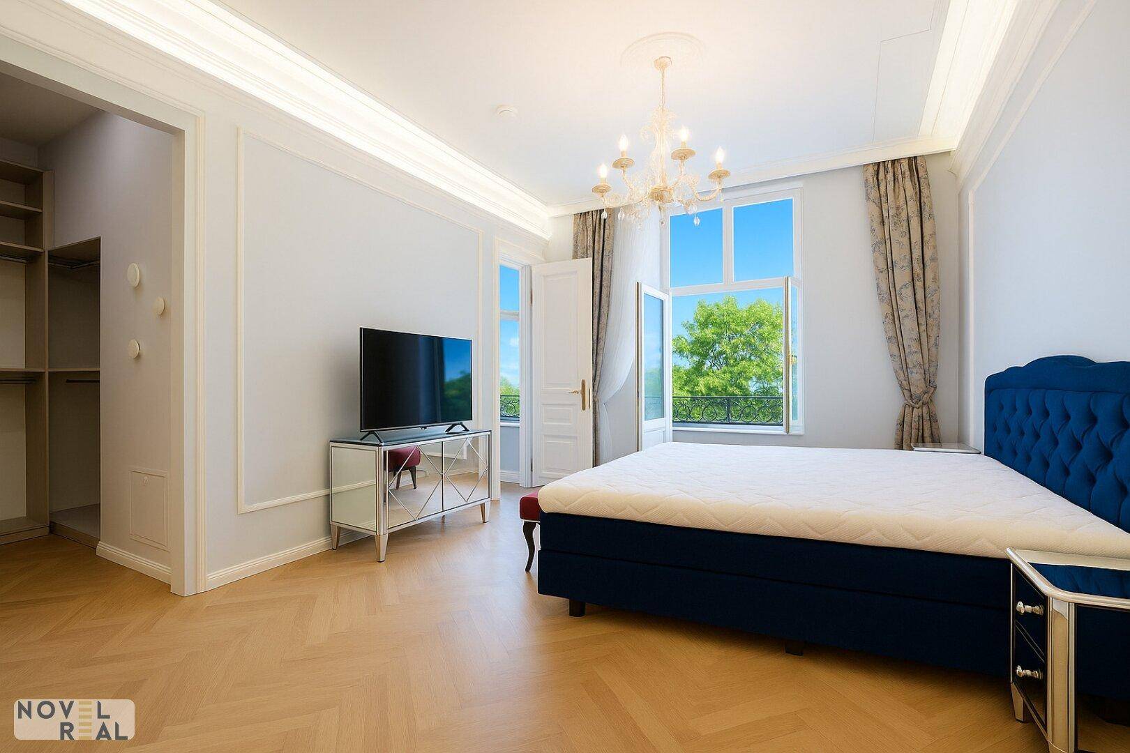 Elegantes Schlafzimmer mit Fischgrätparkett, blauem Bett und Zugang zum Balkon.