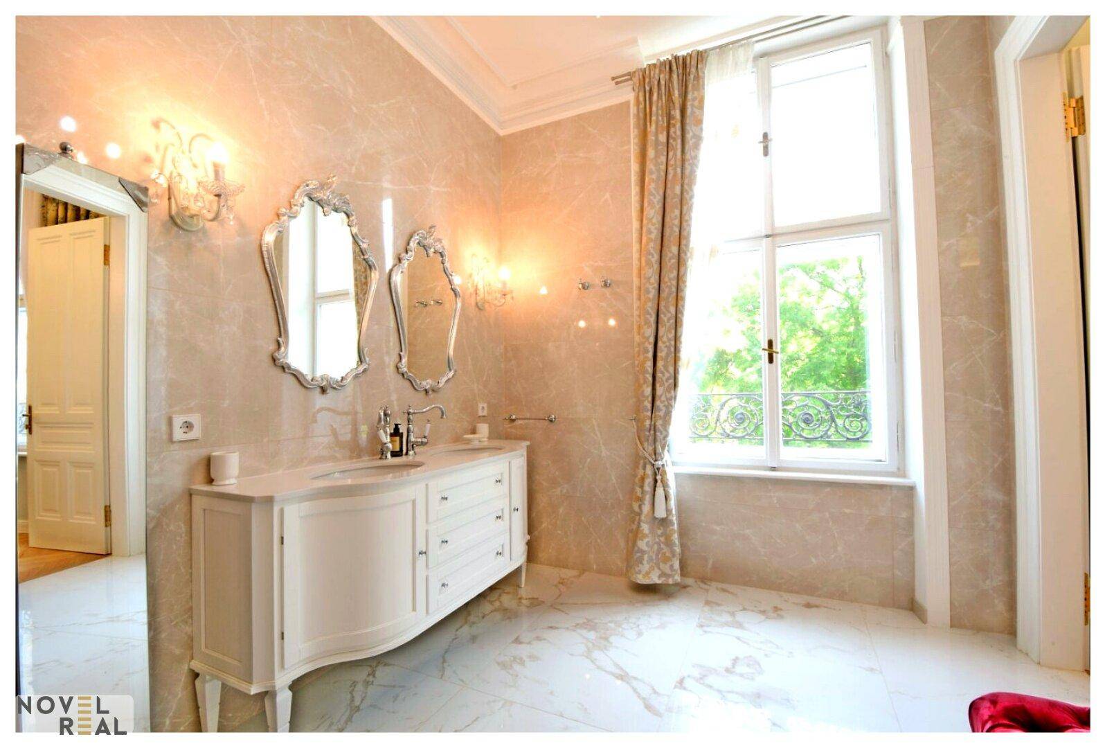 Luxuriöses Badezimmer mit Doppelwaschbecken, Marmorfliesen und großem Fenster.