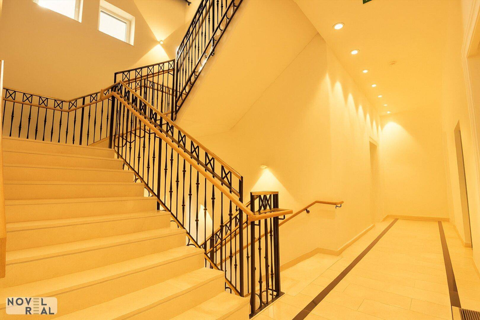 Helles Treppenhaus mit elegantem Geländer, Holzhandlauf und indirekter Beleuchtung.