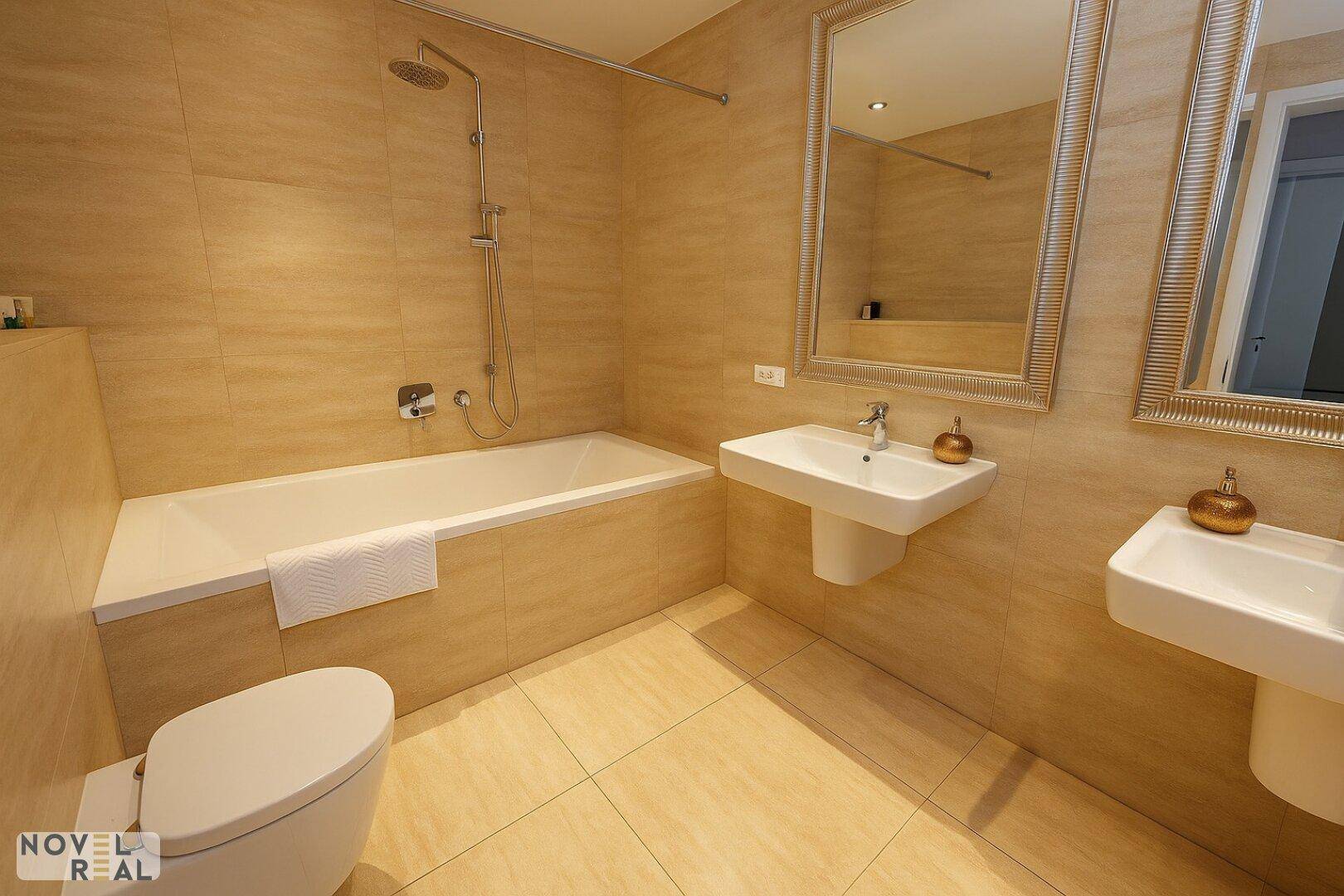 Badezimmer mit Badewanne, zwei Waschbecken und beigefarbenen Fliesen.