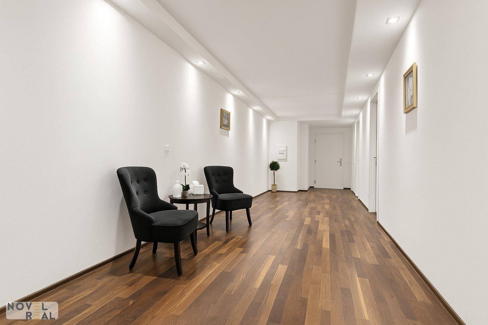 Langer, heller Flur mit Holzboden und einer kleinen Sitzgelegenheit.