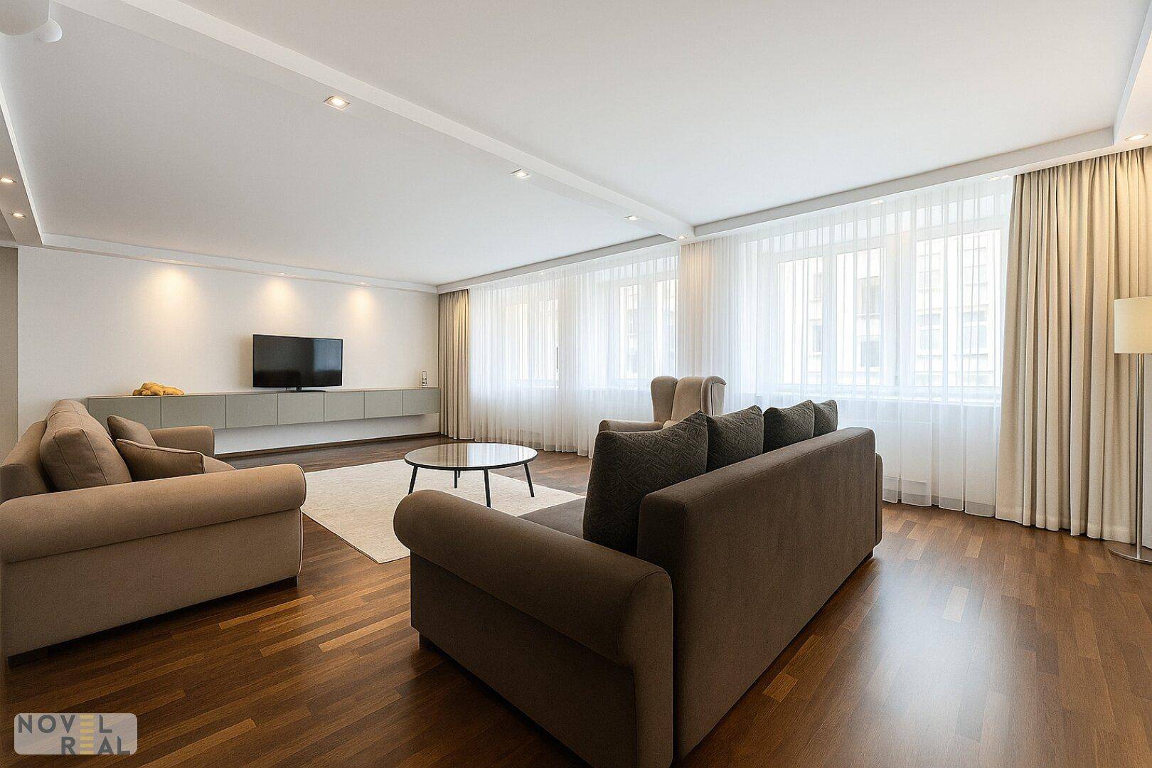 Helles Wohnzimmer mit großen Fenstern, bequemen Sofas und einem modernen TV-Möbel.
