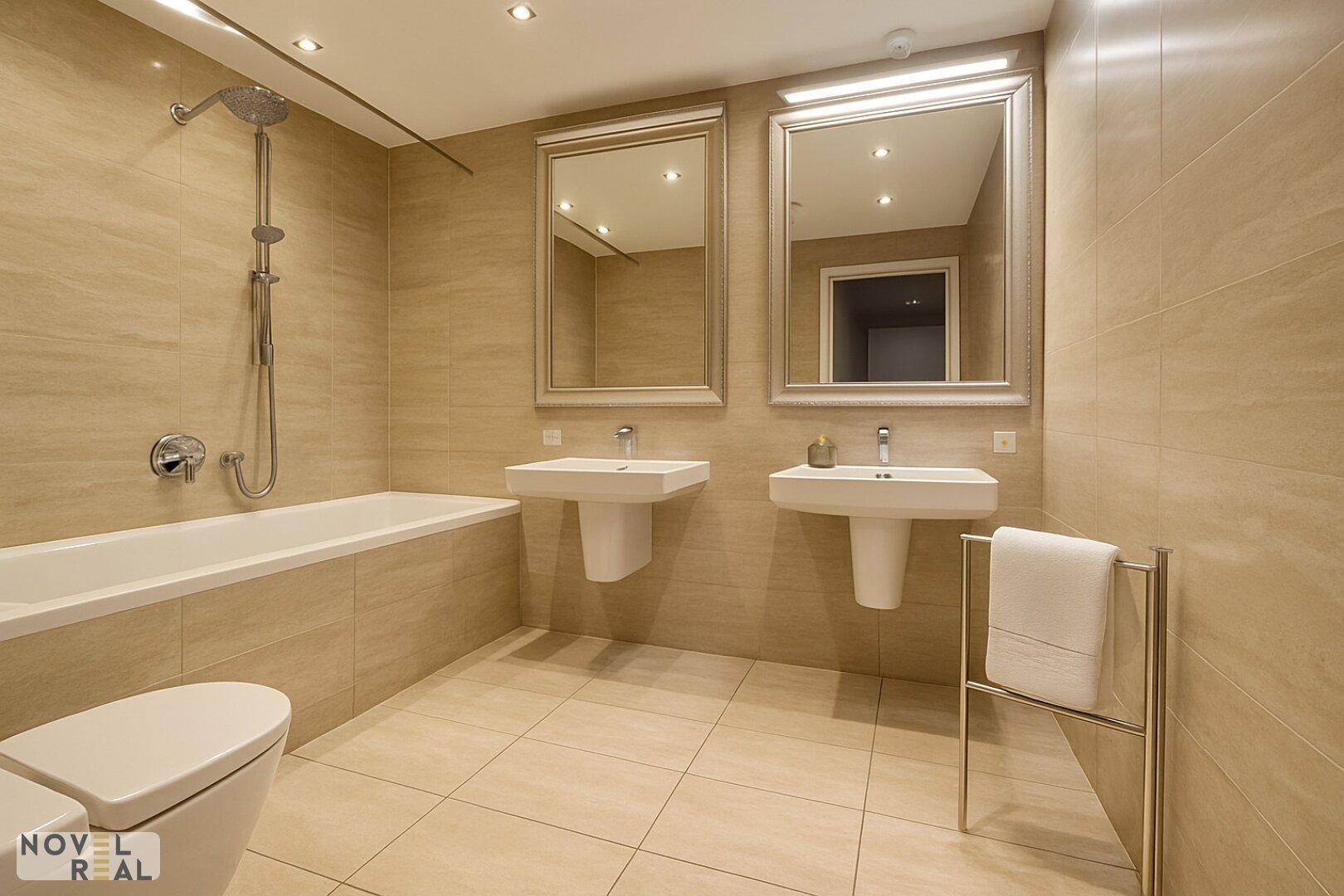 Badezimmer mit Badewanne, zwei Waschbecken, Toilette und beheiztem Handtuchhalter.