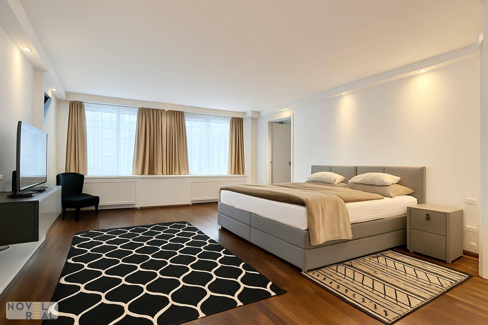 Helles Schlafzimmer mit großen Fenstern, bequemem Bett und modernem TV-Möbel.