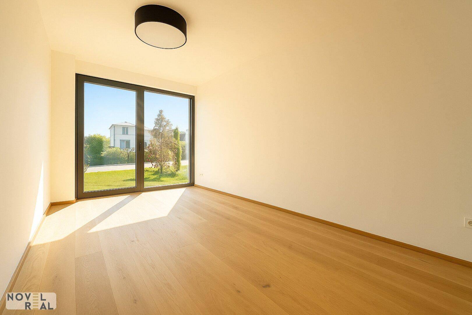 Sonniger Raum mit großen Fenstern, Holzboden und Blick ins Grüne, ideal als Schlafzimmer oder Büro.