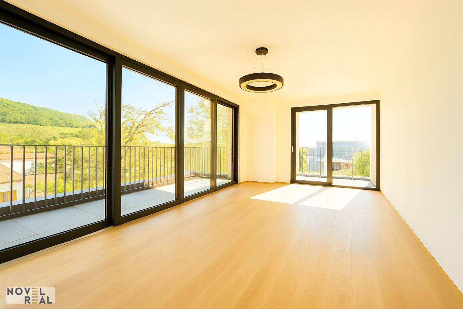Heller Wohnraum mit Zugang zu einem Balkon, großen Fenstern und weitem Blick in die Landschaft.