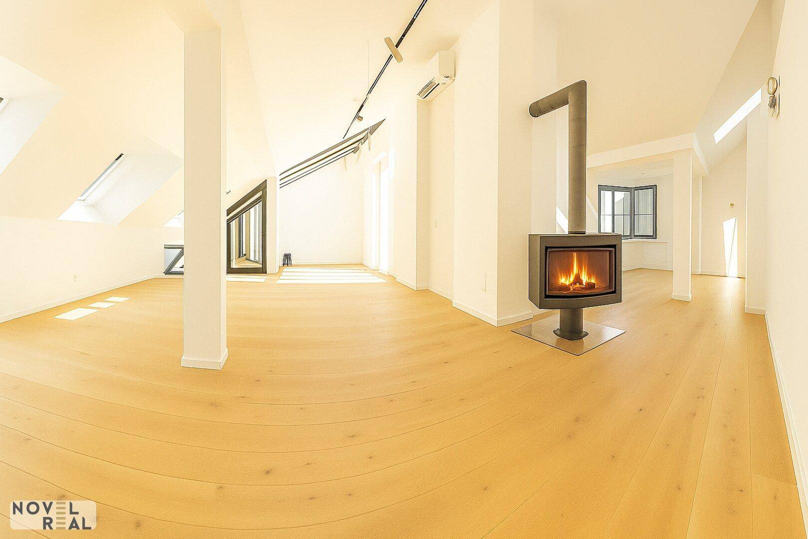 Geräumiger Wohnbereich mit Holzboden, Kamin und schrägen Decken, lichtdurchflutet.