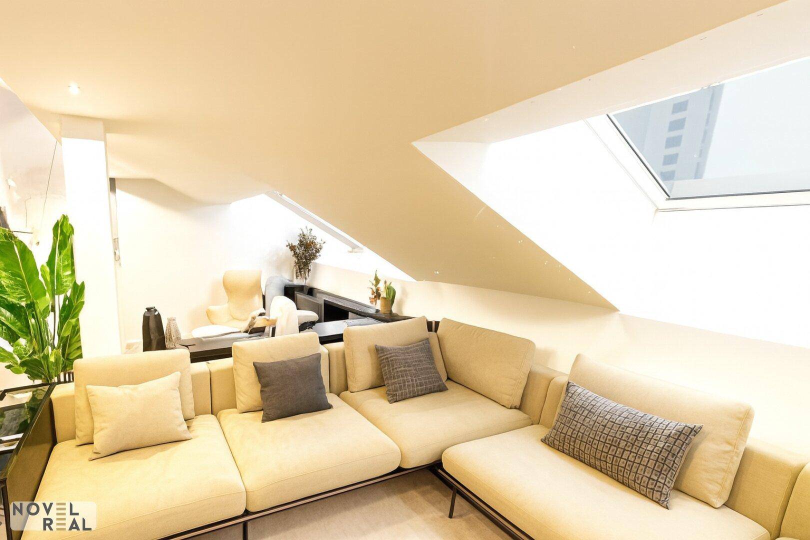 Gemütlicher Wohnbereich mit beigem Sofa, Pflanzen und einem Dachfenster, das viel Licht spendet.