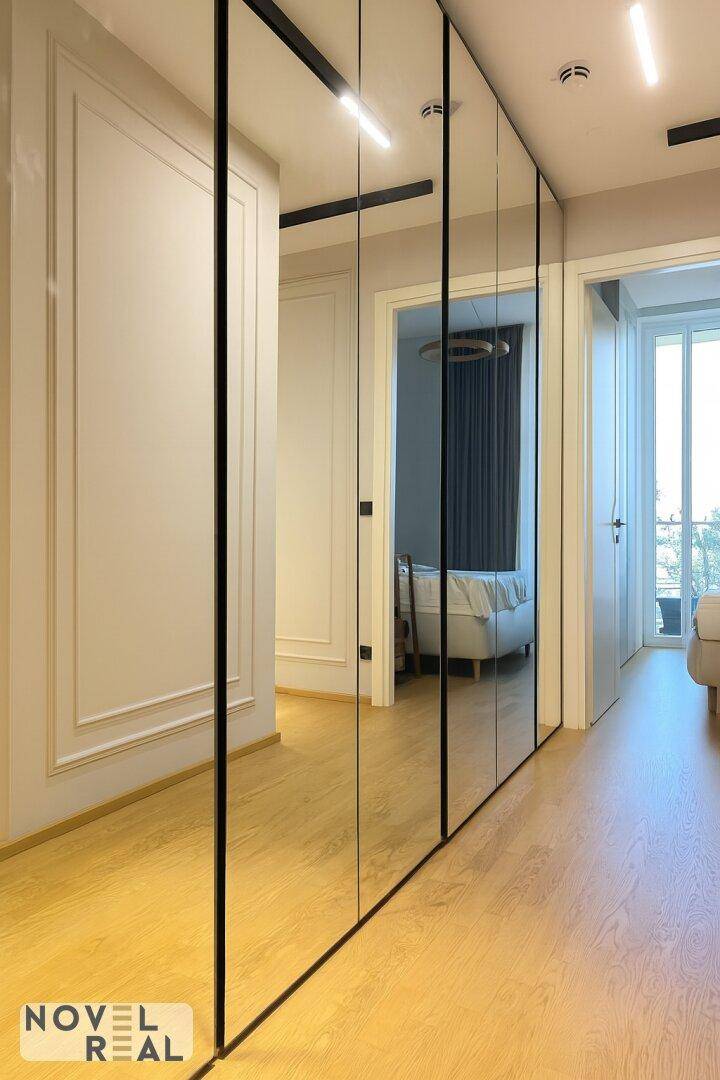 Heller Flur mit durchgehenden Spiegelschränken und Holzboden, der zu den Zimmern führt.