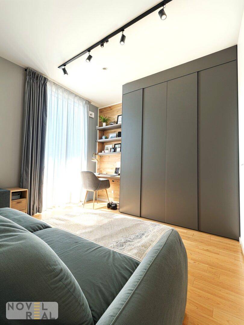 Schlafzimmer mit integriertem Arbeitsbereich, grauem Sofa und Einbauschränken.