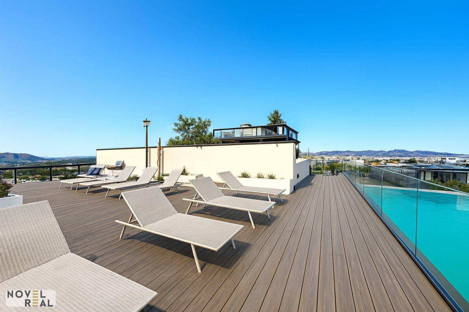 Geräumige Dachterrasse mit vielen Liegestühlen und einem Poolbereich unter blauem Himmel.