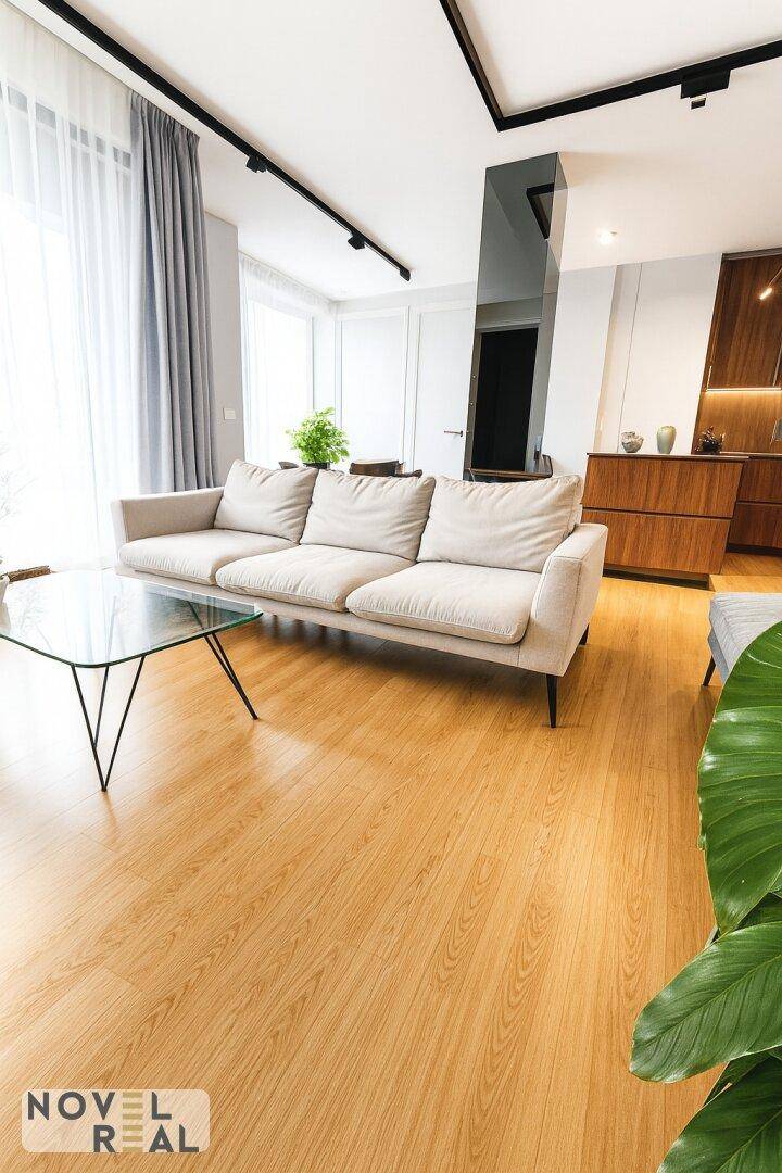 Helles Wohnzimmer mit beigem Sofa, Glas-Couchtisch und Holzfußboden.