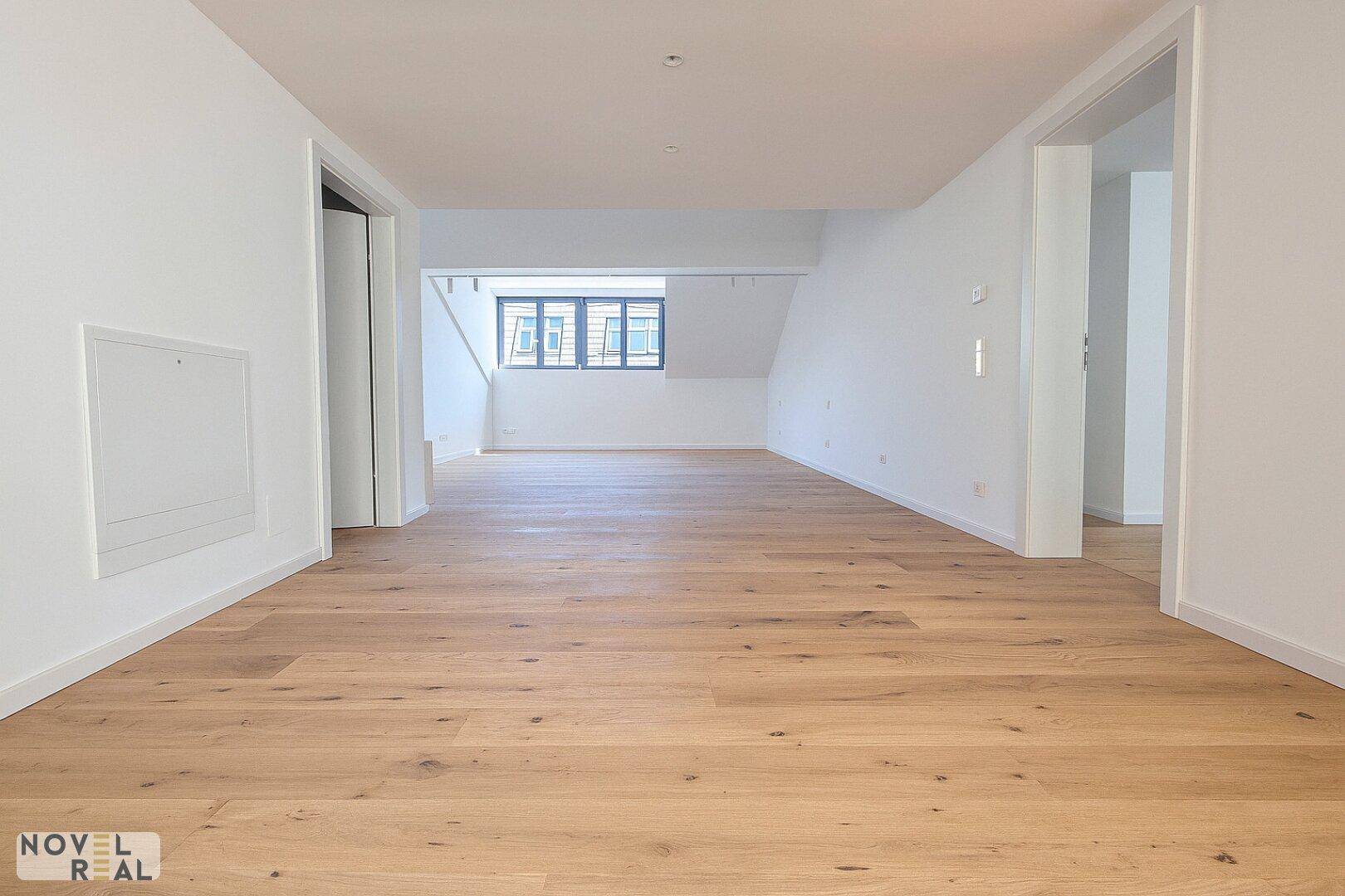 Geräumiger, leerer Raum mit Holzboden und einem Fenster, das Tageslicht hereinlässt.