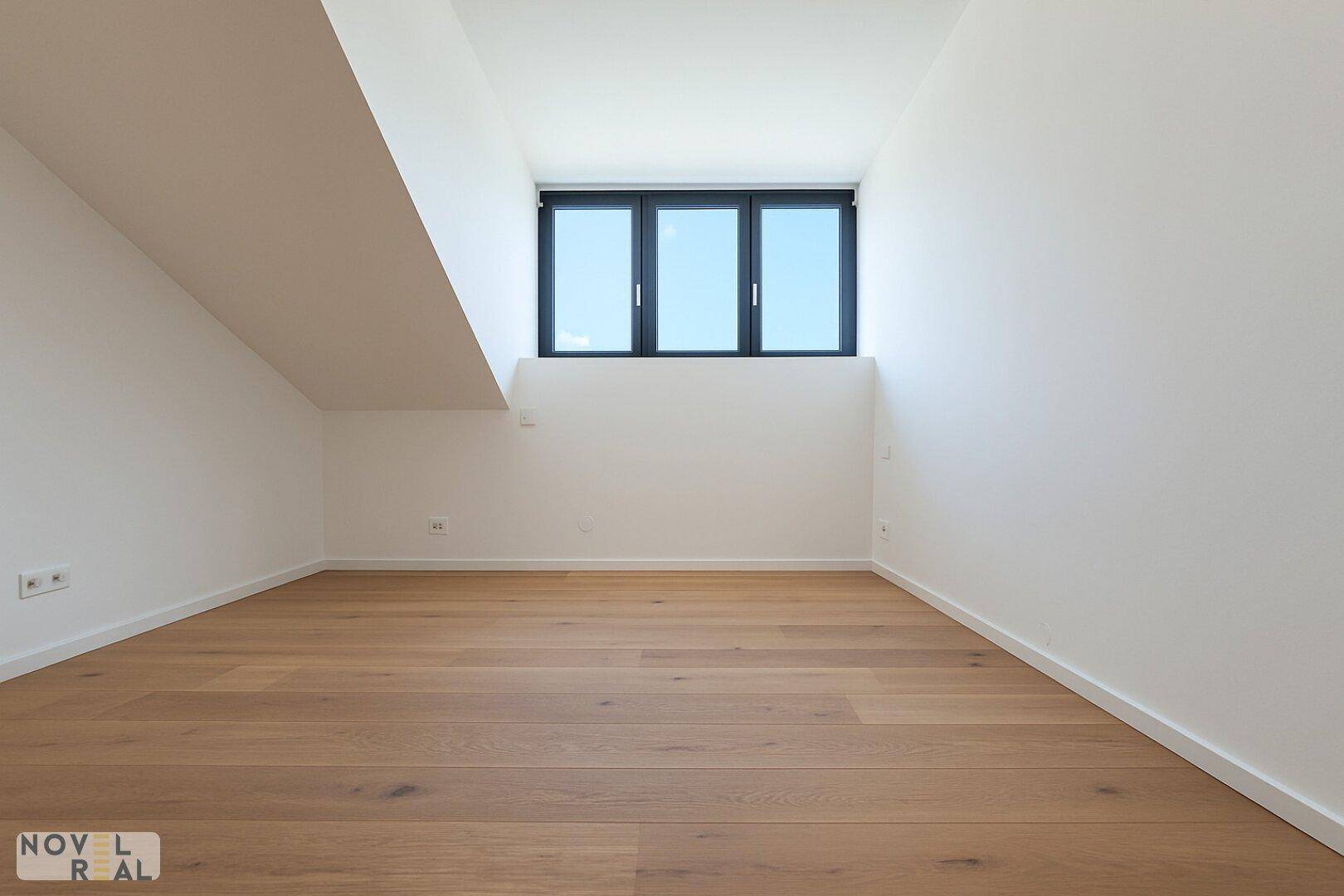 Schlichter Raum mit Holzboden und einem Fenster, das eine ruhige Atmosphäre schafft.